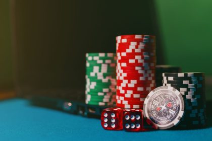 Fichas de cassino e dados sobre uma mesa, ao lado de um laptop, em referência a apostas online