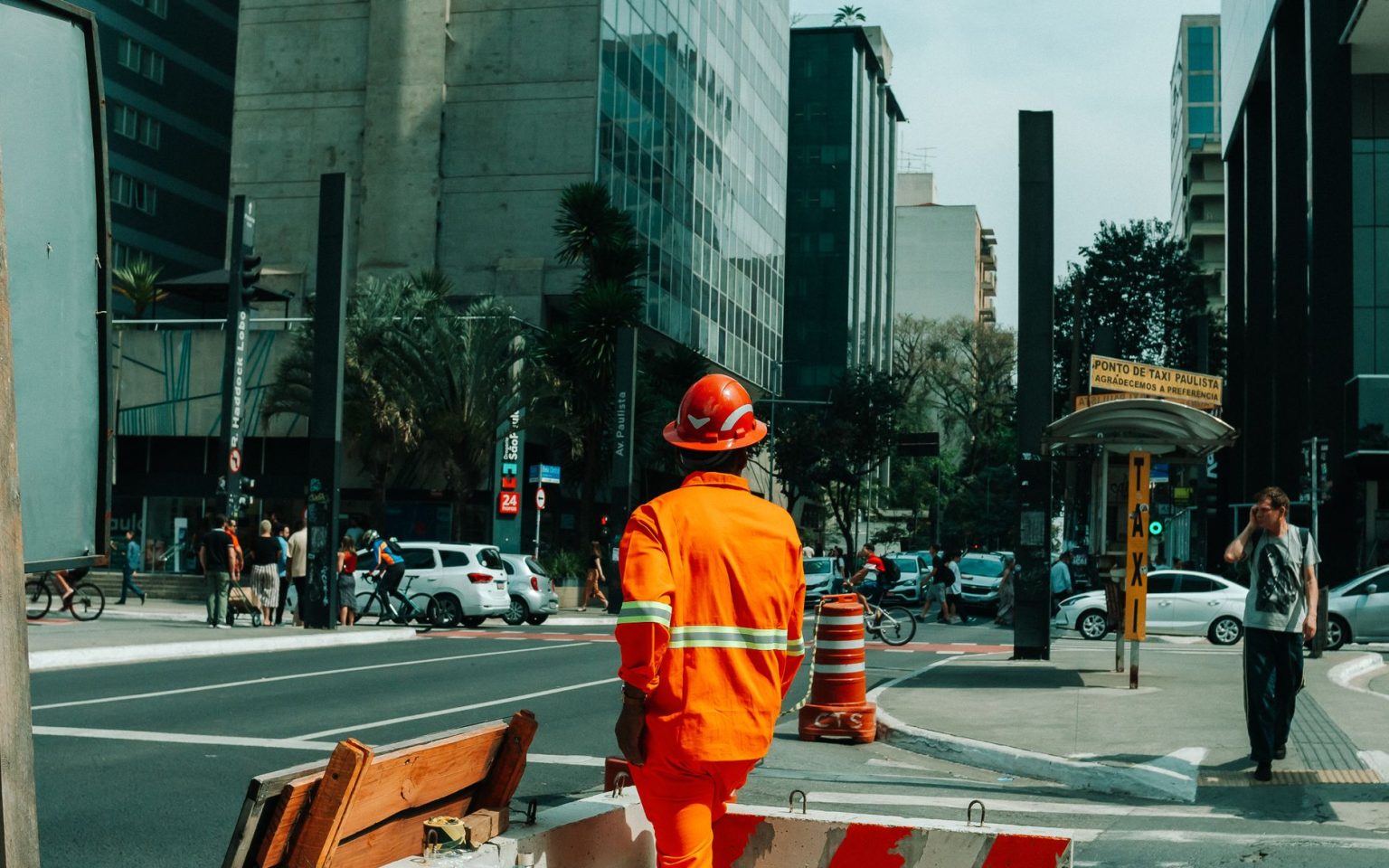 Trabalhador da construção civil caminha por uma rua movimentada de São Paulo durante o horário comercial.