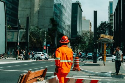 Trabalhador da construção civil caminha por uma rua movimentada de São Paulo durante o horário comercial.