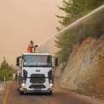 Bombeiros usam o canhão de água de um caminhão para combater um incêndio florestal.
