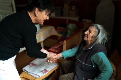 Duas mulheres idosas se cumprimentam em casa, em uma cena de cuidado e companhia.