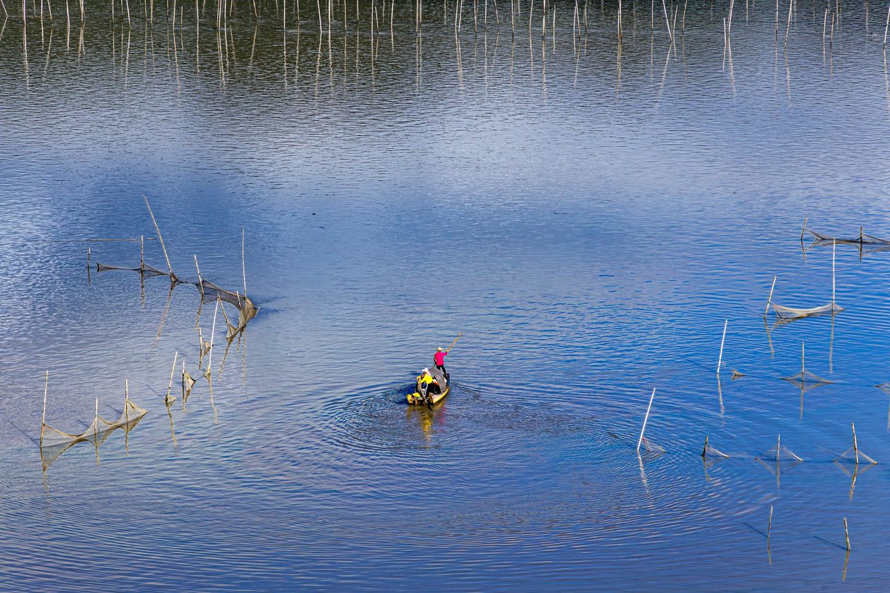Pequeno barco de pesca navega por um lago com redes tradicionais.