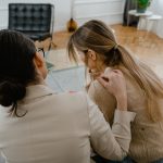 Duas mulheres sentadas em ambiente interno, em um momento de apoio e empatia.