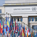 Bandeiras de vários países diante do escritório das Nações Unidas em Genebra, simbolizando a cooperação internacional.