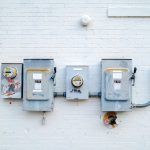 Medidores e caixas de energia instalados em uma parede de tijolos brancos.