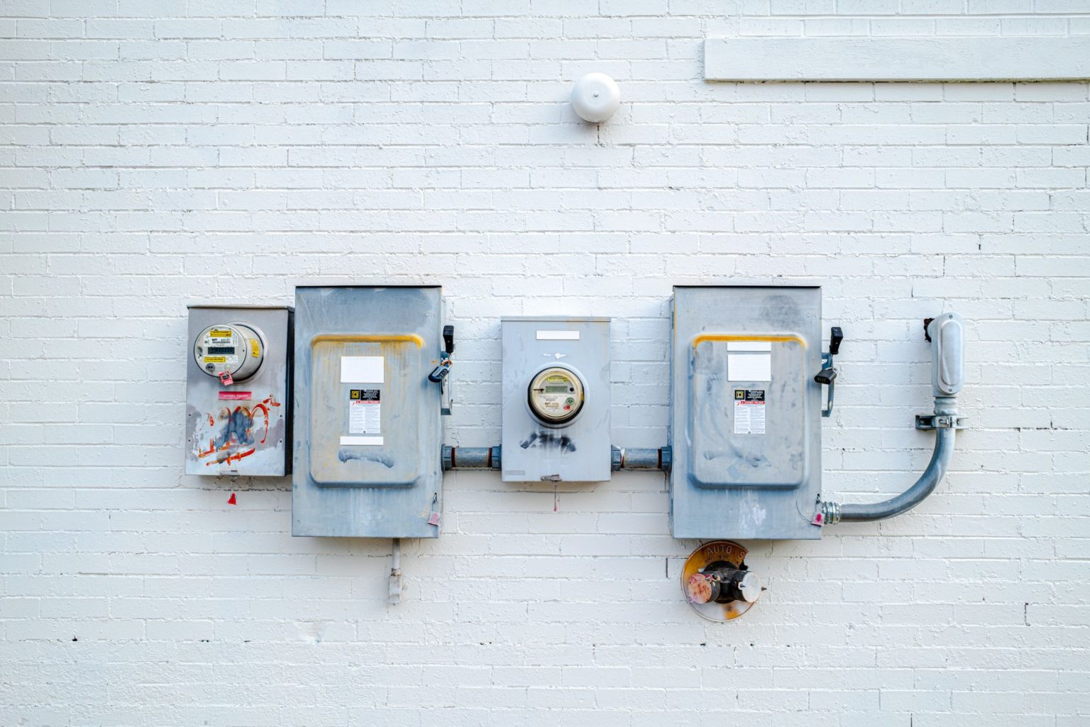 Medidores e caixas de energia instalados em uma parede de tijolos brancos.