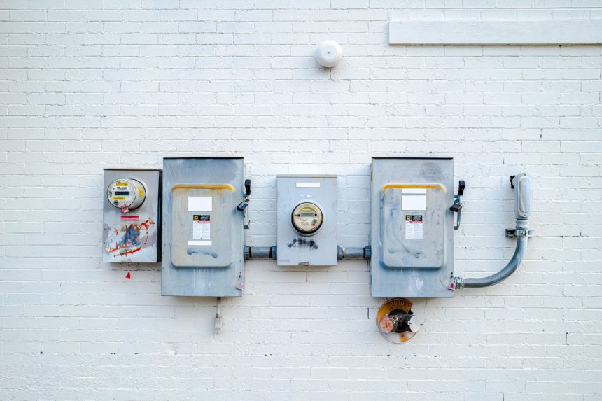 Medidores e caixas de energia instalados em uma parede de tijolos brancos.