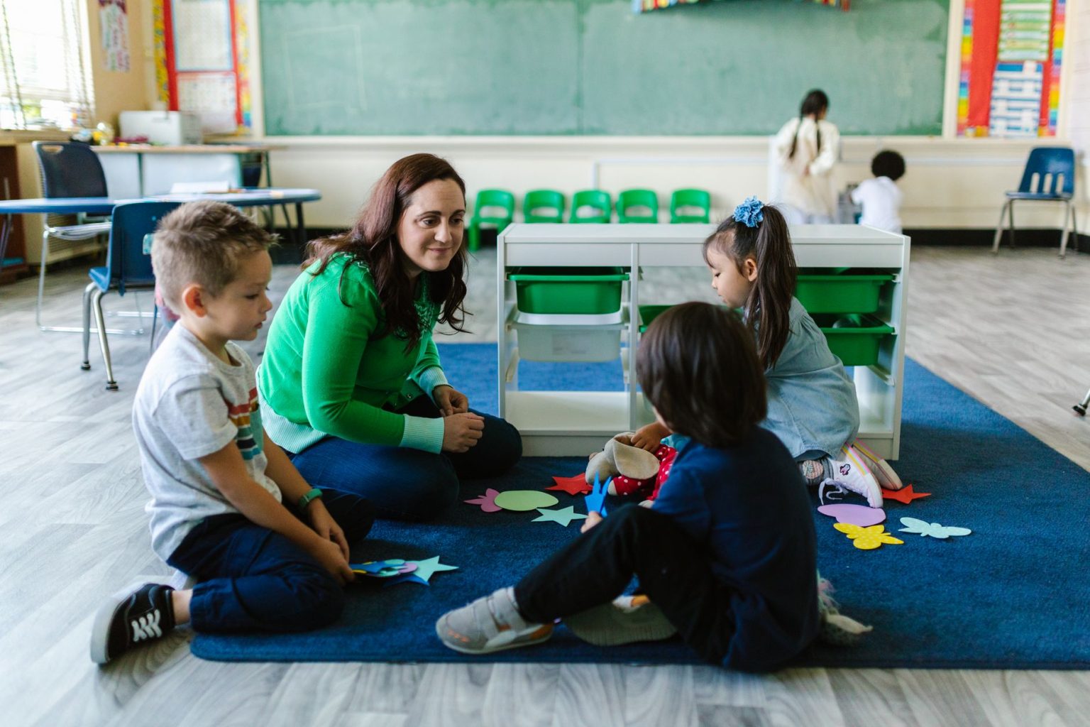 Professora realiza atividade educativa com crianças sentadas no chão de uma sala de aula.